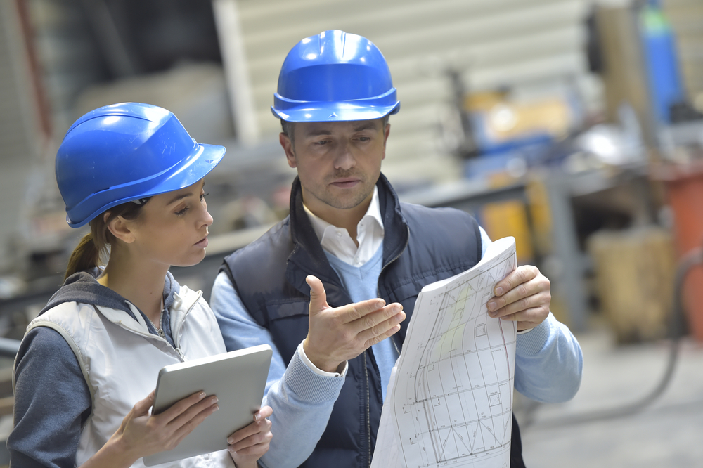 A worker and consultant review documents on production floor.